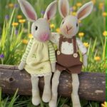 Para ręcznie szydełkowanych króliczków amigurumi – ona w żółtej sukience, on w brązowych spodenkach – siedząca na kłodzie drewna na łące.